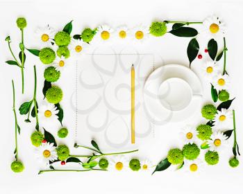 Paper, pencil and cup for coffee or tea with wreath frame from chamomile and chrysanthemum flowers, ficus leaves and ripe rowan on white background. Overhead view. Flat lay.