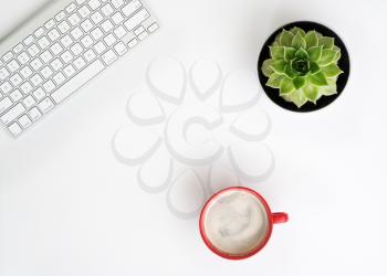 White office desk table with wireless aluminum keyboard, cup of coffee and succulent flower in pot. Top view with copy space. Flat lay. 