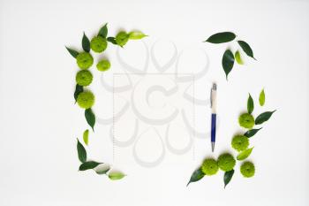Paper and pen with decoration of chrysanthemum flowers and ficus leaves on white background. Overhead view. Flat lay.