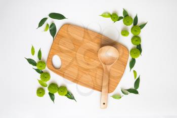Wooden cutting board and ladle with decoration of chrysanthemum flowers and ficus leaves on white background. Overhead view. Flat lay.