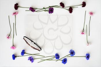Glasses and paper with wreath frame from wildflowers on white background. Overhead view. Flat lay.