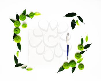 Paper and pen with decoration of chrysanthemum flowers and ficus leaves on white background. Overhead view. Flat lay.