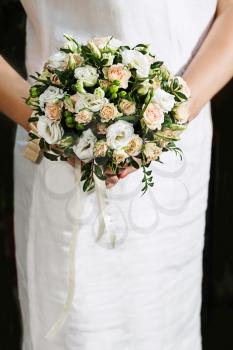 Colorful bridal beautiful bouquet of roses different colors and other flowers in hands of bride in white dress.