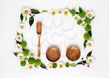 Wooden scoop, plates and space for your text or product with decoration of chrysanthemum flowers and ficus leaves on white background. Overhead view. Flat lay.
