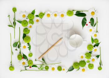 Paper, pencil and cup for coffee or tea with wreath frame from chamomile and chrysanthemum flowers, ficus leaves and ripe rowan on white background. Overhead view. Flat lay.