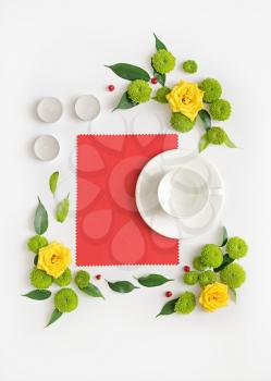 Paper, candles and cup for coffee or tea with wreath frame from roses, chamomile and chrysanthemum flowers, ficus leaves and ripe rowan on white background. Overhead view. Flat lay.