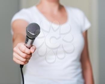 Close up of woman in white shirt, which offers someone to give her an interview. Holding microphone in his hand. 