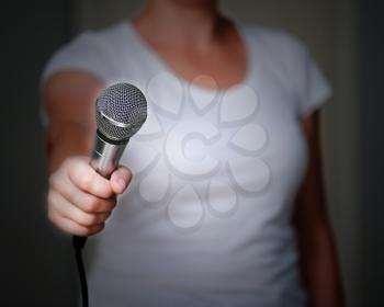 Close up of woman in white shirt, which offers someone to give her an interview. Holding microphone in his hand. 