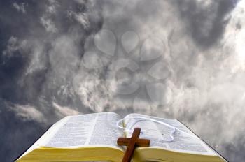 Royalty Free Photo of an Open Bible With a Cross on It Against Clouds