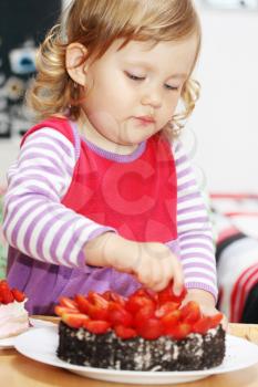 The little girl eating cake with strawberries