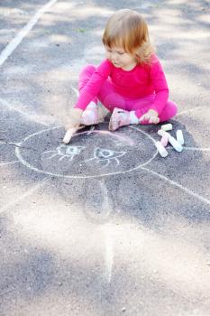 Little girl draws a large sun on asphalt
