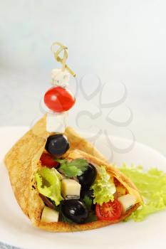 Pancake stuffed with salad, cheese, tomatoes and olives