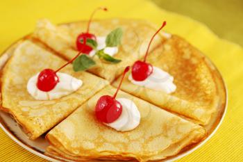 Pancakes with cream and cherries on a plate
