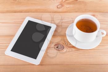 Tablet computer and a cup of tea on a wooden table.