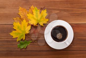 Coffee cup and autumn leaves on a wooden background.