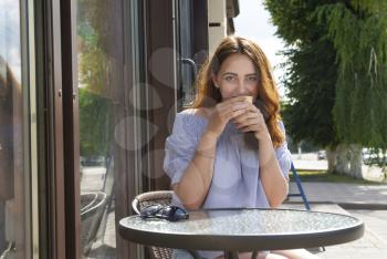 Young girl drinking coffee in a cafe in the street.