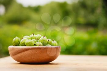 Old Wooden Bowl Filled With Succulent Juicy Fresh Ripe Green Gooseberries On An Old Wooden Table Top. Green Background