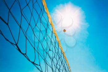 Volleyball Ball Over Net On Background Of Blue Summer Sunny Sky. Ball Flying Through Air On Beach