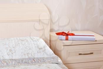 flat gift box with red bow lying on the nightstand next to the bed