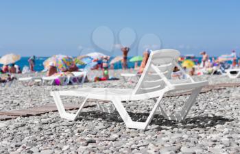 white plastic lounger on the beach by the sea on the background of people sunbathing