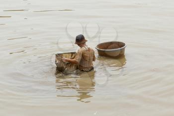 A vietnamese fisherman is searching for shells in the water in Saigon