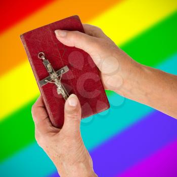 Old hands (woman) holding a very old bible, rainbow flag pattern