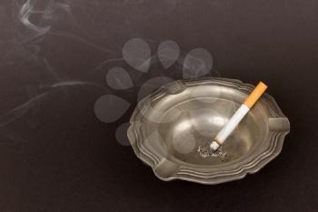 Burning cigarette in an old tin ashtray, isolated