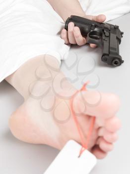 Woman committed suicide, under a sheet with a toe tag, selective focus on gun