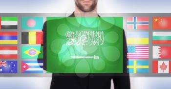 Hand pushing on a touch screen interface, choosing language or country, Saudi Arabia
