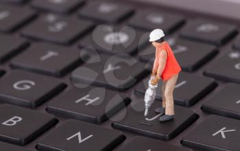 Miniature worker with drill working on a computer keyboard
