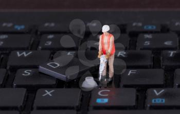 Miniature worker with drill working on a computer keyboard