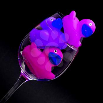 Pink and purple rubber ducks in wineglasses, dark background