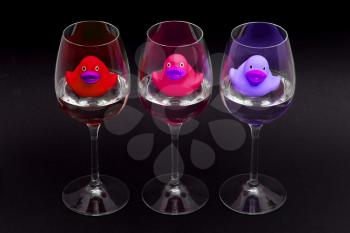 Red, pink and purple rubber ducks in wineglasses, dark background
