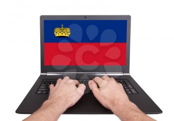 Hands working on laptop showing on the screen the flag of Liechtenstein
