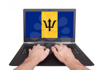 Hands working on laptop showing on the screen the flag of Barbados