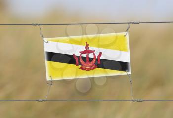 Border fence - Old plastic sign with a flag - Brunei