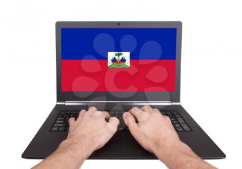 Hands working on laptop showing on the screen the flag of Haiti