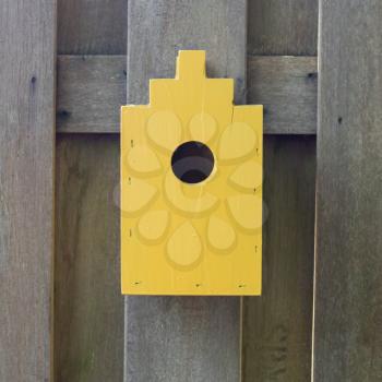 Yellow birdhouse on a wooden fence in a garden