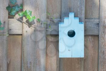 Blue birdhouse on a wooden fence in a garden