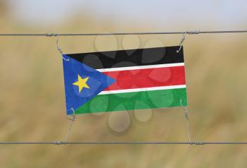 Border fence - Old plastic sign with a flag - South Sudan