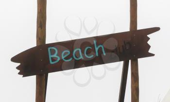 Brown sign saying 'Beach' - Grey sky in the background