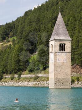 Submerged tower of reschensee church, man swimming next to it -  South Tyr or Alto Adige in Bolzano or bozen at Italy