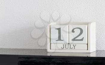 White block calendar present date 12 and month July on white wall background