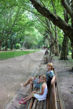 mother and daughter sitting on the bench in park with greater trees