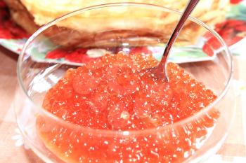 red caviar in a plate with the spoon and pancakes on a background