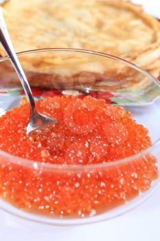 red caviar in a plate with the spoon and pancakes on a background