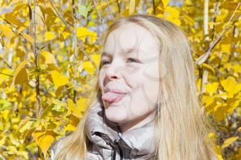 Autumn portrait of blond girl in sunlight put out tongue