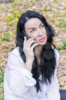 Caucasian brunette talking by cellular in autumn park