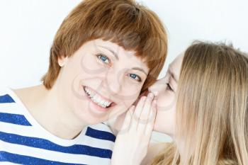 Daughter says a secret an her mother ear on white wall