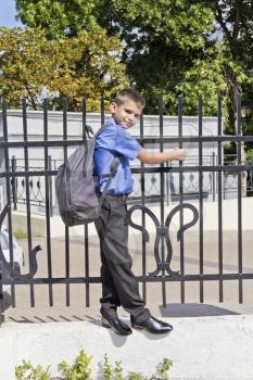 Cute boy are hanging on the fence with school backpack